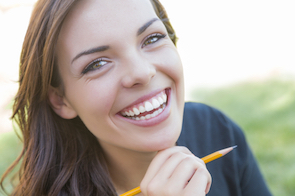 Portrait of Pretty Young Female Student with Pencil on Campus Lawn.